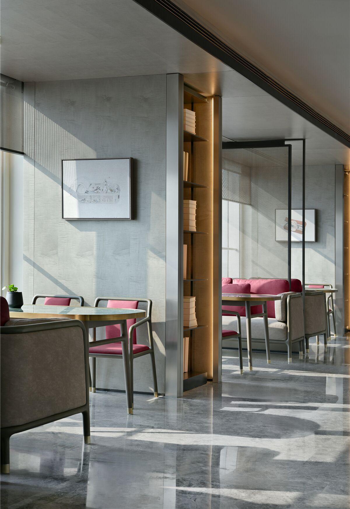 A modern restaurant interior with a minimalist design, featuring a central seating area with cushioned benches and tables, a patterned wall, and a framed artwork on the wall.
