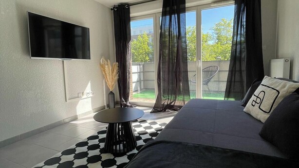 A modern bedroom with a bed, a flat-screen TV, a small round table, and a view of the outdoors through large windows.