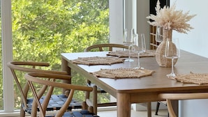 A wooden dining table with woven placemats, two chairs, and a vase with dried flowers. - New Luxury Beachfront Escape with Pool and Hottub (Kelowna)