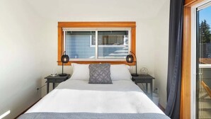Un dormitorio con una cama grande, dos mesitas de noche, una ventana con persianas y vistas al exterior.