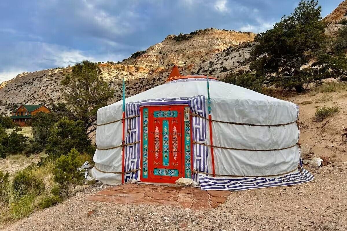 A traditional yurt with a red door, surrounded by a mountainous landscape.