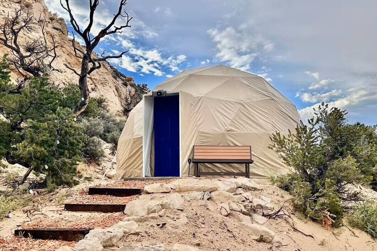 A dome-shaped tent with a blue door, surrounded by rocky terrain and sparse vegetation.