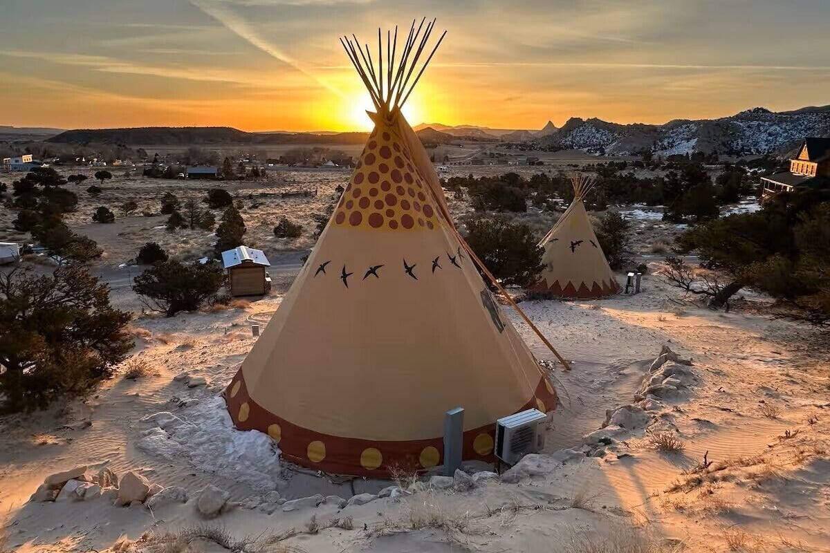 A snow-covered landscape with two tipi-style tents, one with a central pole and another with a decorative design.