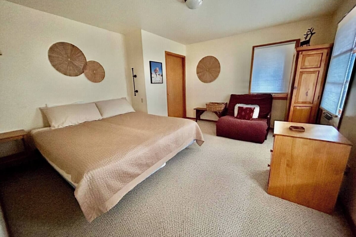 A bedroom with a bed, a chair, a dresser, and a window.