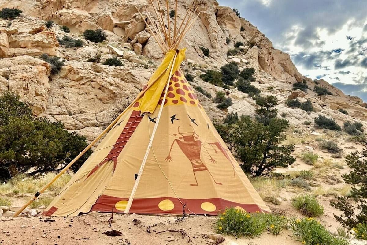 A tipi with a painted design, set against a rocky desert landscape.