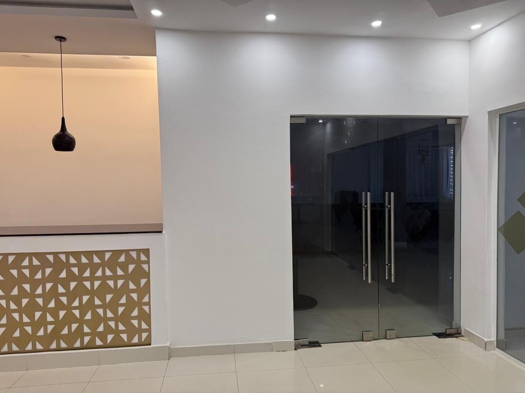 Un interior moderno con puerta de vidrio de entrada, pared con diseño geométrico y una lámpara colgante.