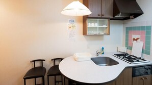 Een compacte keuken met een rond kookeiland, twee barkrukken, een gasfornuis, een spoelbak en een kast met een glazen deur.