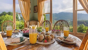 A breakfast table with fruit, muffins, and juice glasses, set against a backdrop of a scenic mountain view. - Sleeps 22 On 17 Acres, River Access, Pet Friendly (Waynesville)