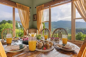 A breakfast table with fruit, muffins, and juice glasses, set against a backdrop of a scenic mountain view. - Sleeps 22 On 17 Acres, River Access, Pet Friendly (Waynesville)