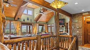 A spacious room with a wooden ceiling, a stone fireplace, and a large window offering a view of the outdoors. - Sleeps 22 On 17 Acres, River Access, Pet Friendly (Waynesville)