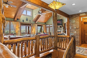 A spacious room with a wooden ceiling, a stone fireplace, and a large window offering a view of the outdoors.