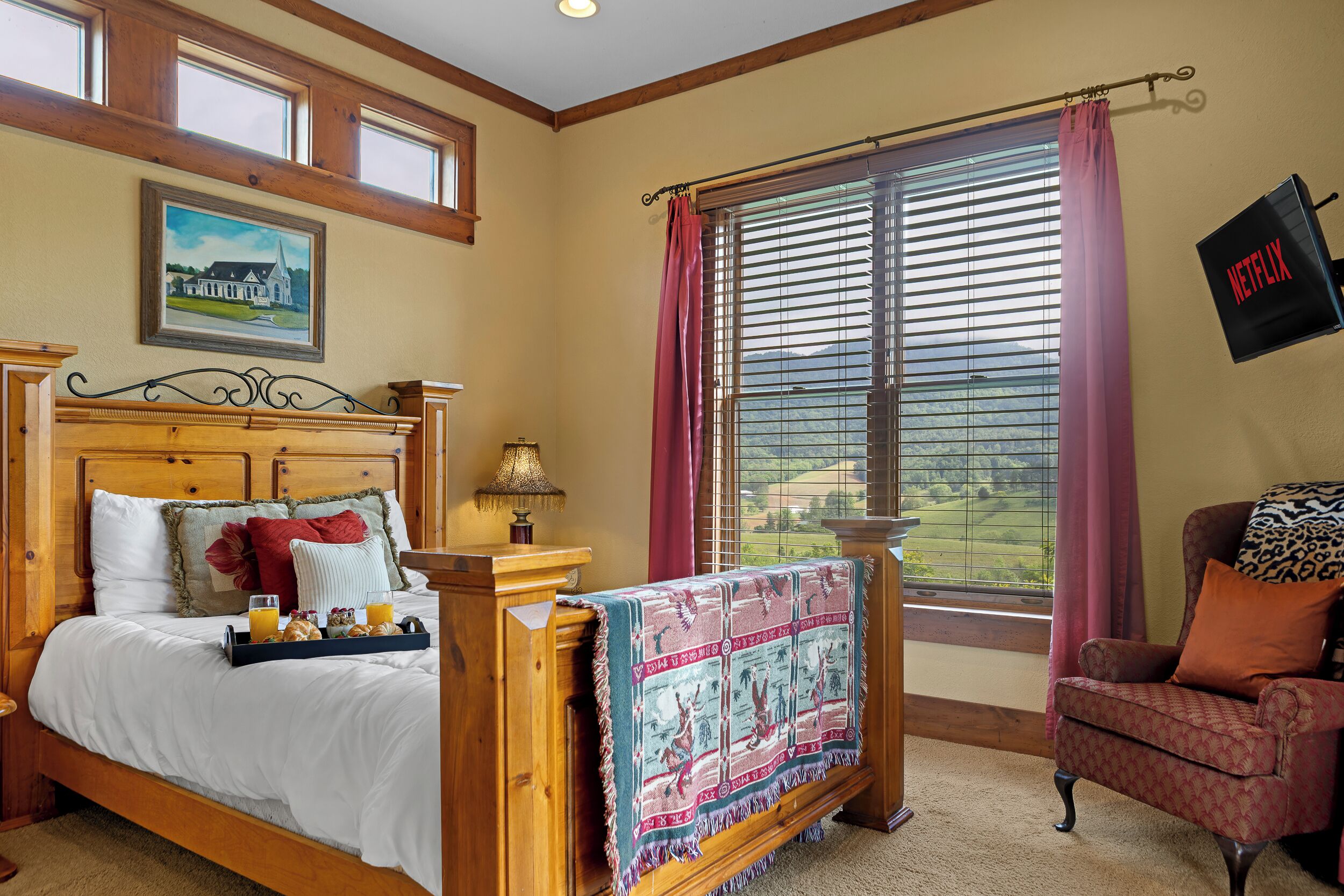 A bedroom with a wooden bed, a bedside table with a lamp, a chair with a leopard print pillow, and a window with blinds.