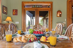 Een ontbijttafel met croissants, fruit en sap, in een kamer met houten meubels en uitzicht door een deuropening.