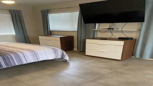 A bedroom with a bed, a dresser, a television, and curtains. - Charming Studio apartment in delightful Pompano Beach 1 block from the ocean (Pompano Beach)