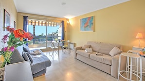 A modern living room with a sofa, a dining table, and a balcony with a view.