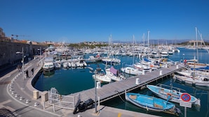 A marina with boats docked, a pedestrian walkway, and a clear blue sky.