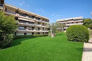 Un immeuble rĂ©sidentiel Ă plusieurs Ă©tages, dotĂ© de balcons, dâune pelouse bien entretenue et surplombant un ciel bleu dĂ©gagĂ©.