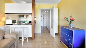 A compact living space with a kitchenette, a dining area with bar stools, a sofa, and a dresser with drawers.