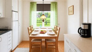 Une cuisine avec une table à manger pour quatre personnes, une machine à café et une vue sur un paysage verdoyant par la fenêtre.
