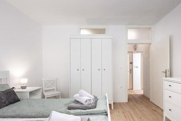 A bedroom with a bed, a nightstand, a chair, a wardrobe, and a dresser.