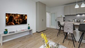 Een moderne keuken met een eethoek, een aan de muur bevestigde televisie en een bankje met decoratieve objecten.