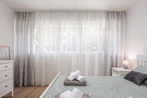 A bedroom with a bed, a nightstand, a dresser, and a window with sheer curtains.