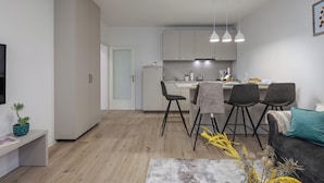 Een moderne keuken met witte kasten, een eethoek met vier stoelen, en een grijze bank met een turquoise kussen.