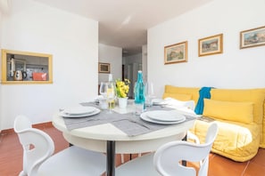 A dining area with a round table, white chairs, and a yellow sofa.