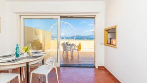 A dining area with a table set for two, a window with a view of a Ferris wheel, and a door leading to an outdoor patio. - Una Finestra Sul Porto, Alghero, Italy (Alghero)
