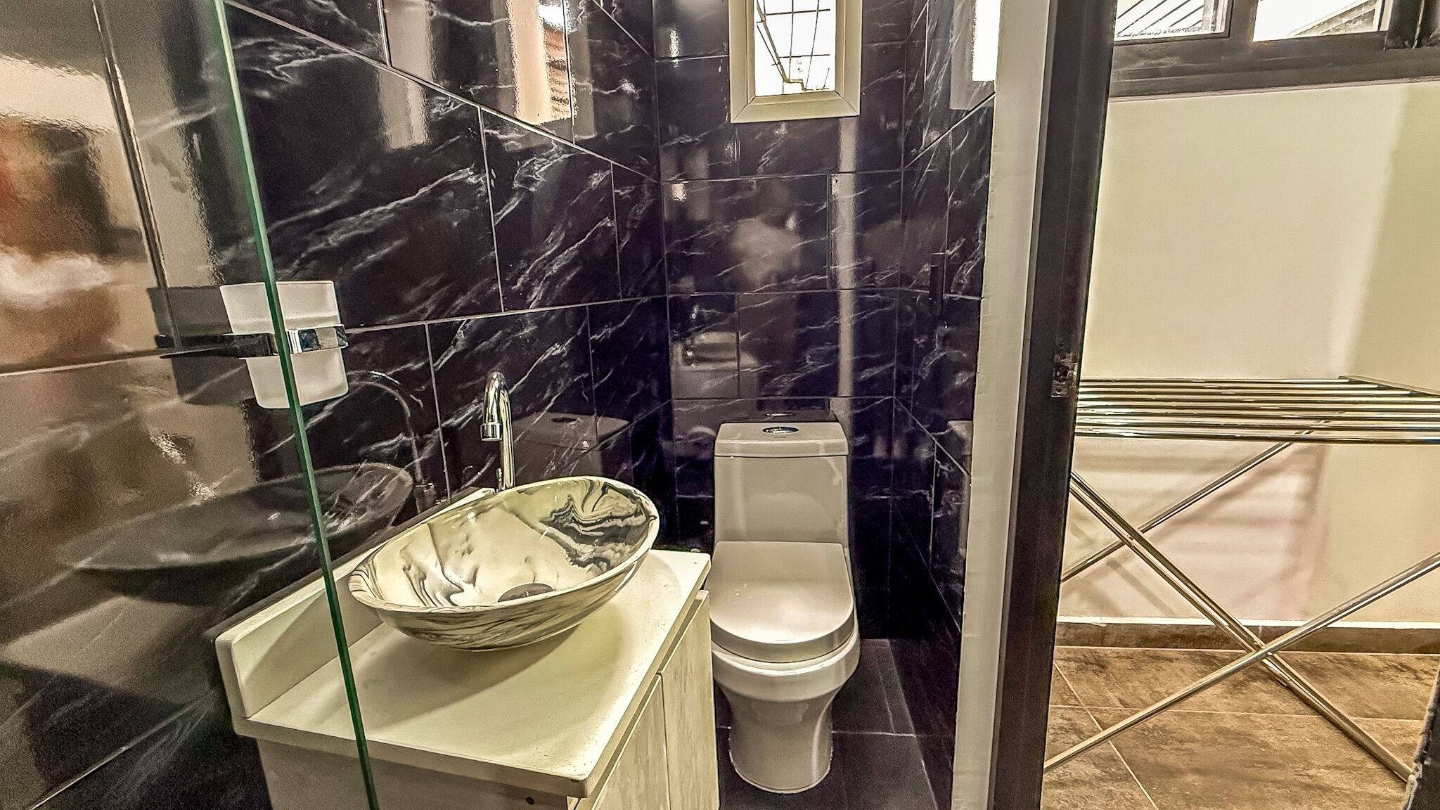 A bathroom with a marble backsplash, a glass sink, and a toilet.