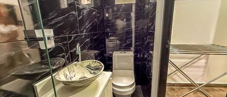 A bathroom with a marble backsplash, a glass sink, and a toilet.