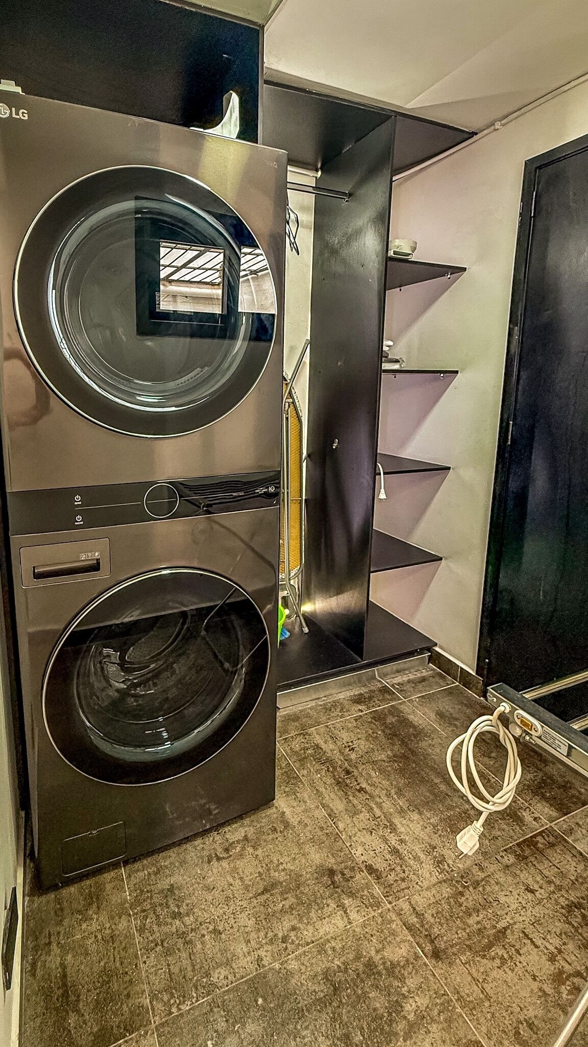 A modern laundry room with two stacked washers and dryers, a tiled floor, and a visible power outlet.