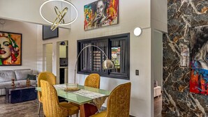 Un comedor con mesa de vidrio, sillas doradas y una lámpara colgante moderna.