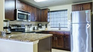 A kitchen with dark wooden cabinets, stainless steel appliances, and a granite countertop. - 3 Free Disney tix! Charming ADA 2-bedroom villa 6 mi. from Disney @ Summer Bay (Clermont)