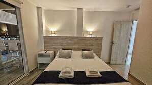 Ett hotellrum med en stor säng, två sänglampor, ett nattduksbord, en garderob och utsikt över omgivningarna genom en skjutdörr.