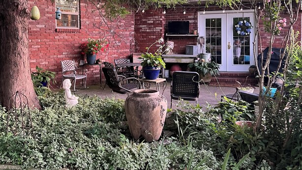 Eine gepflasterte Terrasse mit Sitzgelegenheit, einem großen Baum und einem Blumentopf.