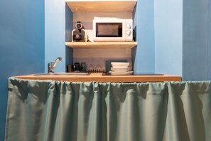Una kitchenette con microondas, hervidor y un pequeño estante con vajilla.