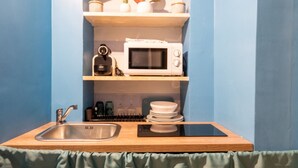 A compact kitchenette with a sink, microwave, and shelves above.