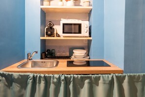 A compact kitchenette with a sink, microwave, and shelves above.