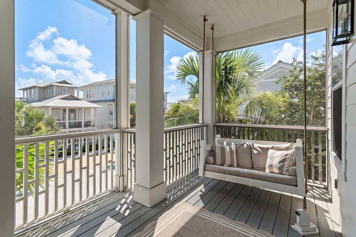 A covered porch with a swing seat, white railings, and a view of neighboring houses and palm trees.