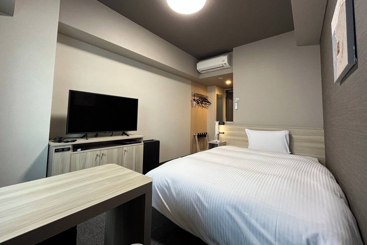 A hotel room with a bed, a TV, a desk, and an air conditioning unit.