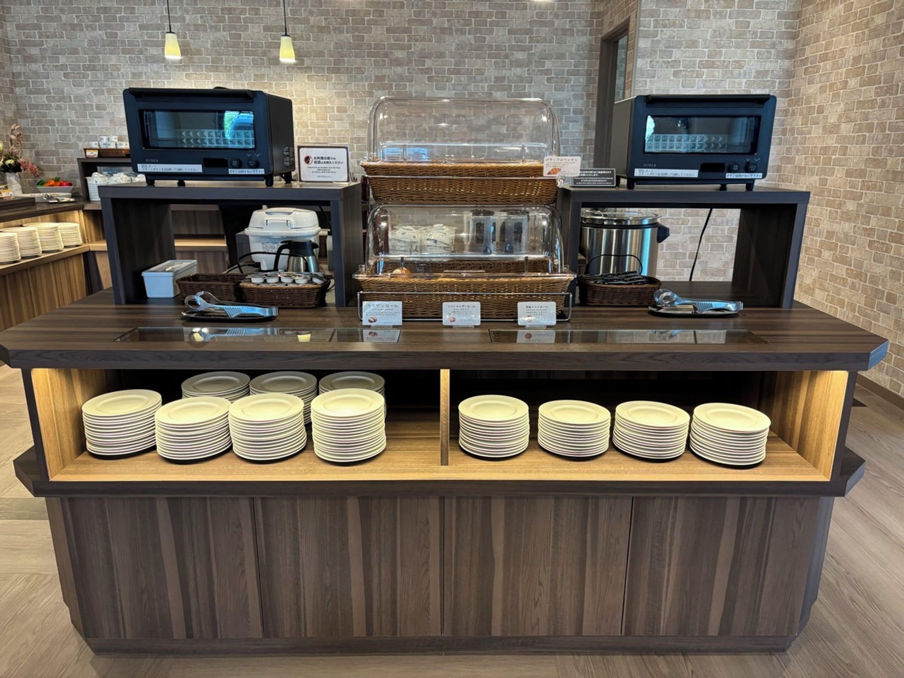 Un mostrador de buffet con dos pantallas de menú digitales, una cafetera y pilas de platos.