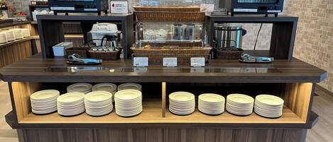 Un mostrador de buffet con dos pantallas de menú digitales, una cafetera y pilas de platos.