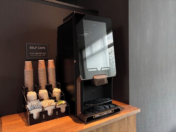 Una estación de café autoservicio con tazas apiladas y una máquina de café.