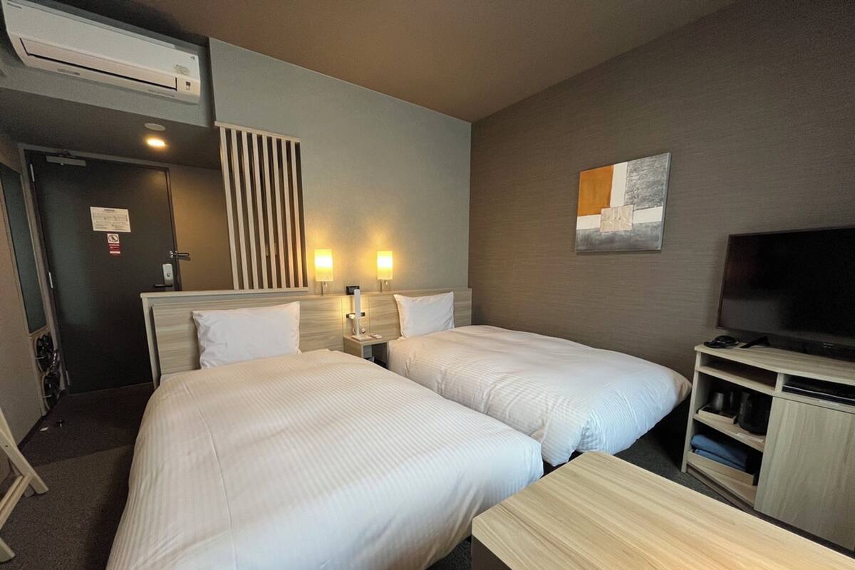 A hotel room with two beds, a TV, and a desk.