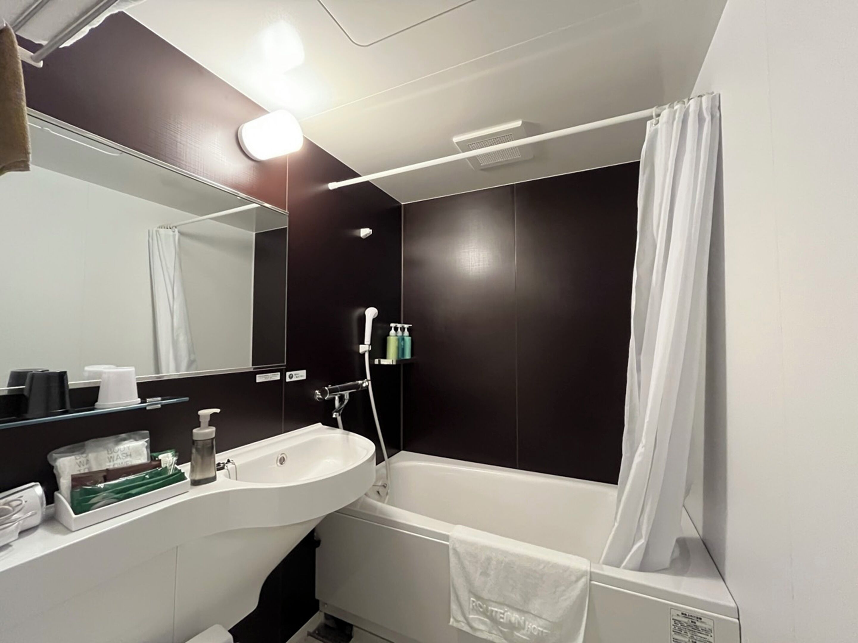A modern bathroom with a white sink, a bathtub, and a shower. There are toiletries on the counter and a towel hanging on the wall.