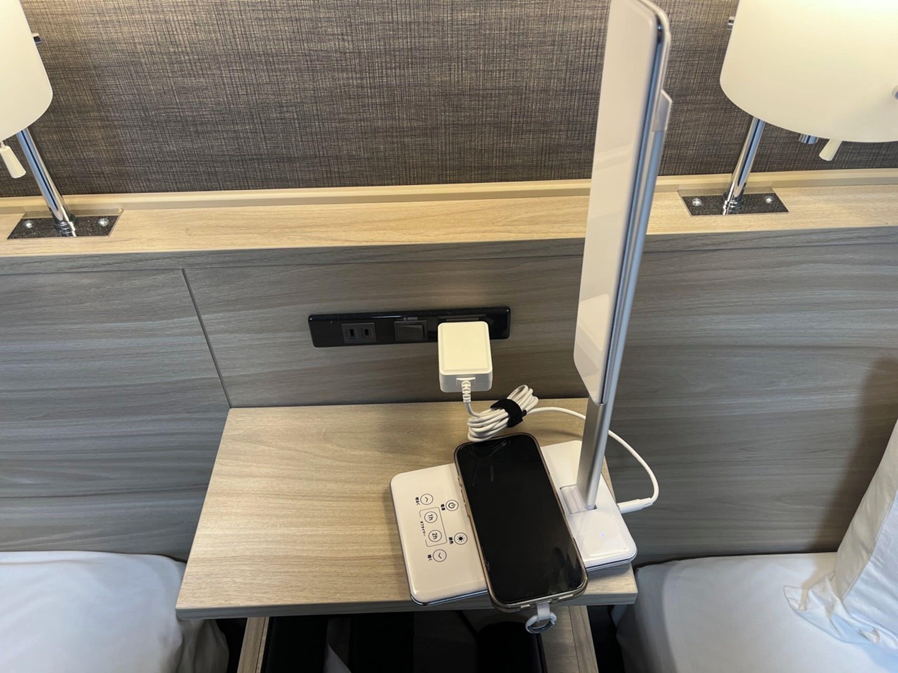 A hotel room with a bedside table, a power outlet, a phone charging station, and two lamps.