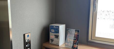 A room with a card reader, a small table with a card and a magazine, and a window with a view of a grid.