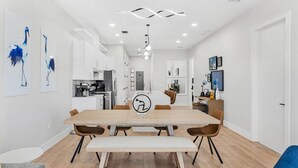 Une cuisine moderne avec des meubles blancs, un îlot central et un coin repas comprenant une table et des chaises en bois.