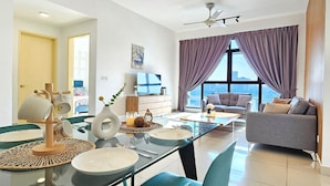 Una sala moderna con una mesa de comedor de vidrio, un sofá y un amplio ventanal con cortinas moradas.